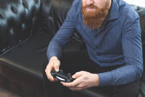 homem com uma barba com fones de ouvido em sua mão joystick em um fundo leve - Foto, Imagem