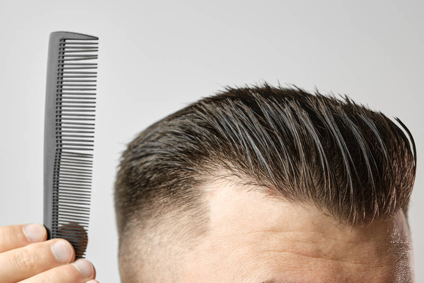 lähikuva nuori mies kampaa hiuksensa muovikammalla. Styling hiukset jälkeen parturi.  - Valokuva, kuva