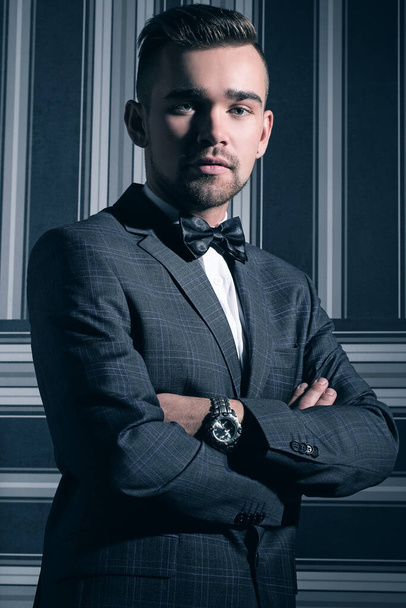 Πορτρέτο ενός όμορφου άντρα με κοστούμι και γραβάτα που ποζάρει πάνω σε ριγέ φόντο - Φωτογραφία, εικόνα