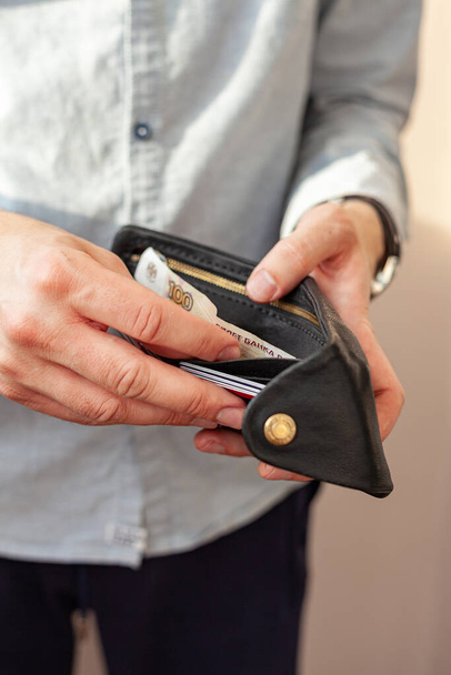 Männliche Hände halten eine Handtasche. Eine Brieftasche mit wenig Geld darin. Das Konzept von Armut und Bankrott - Foto, Bild