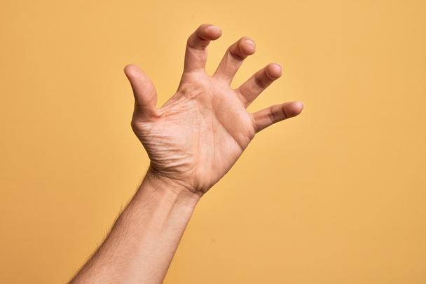 Ręka białego młodzieńca pokazuje palce nad odizolowanym żółtym tłem chwytając się agresywnych i przerażających palców, przemocy i frustracji - Zdjęcie, obraz