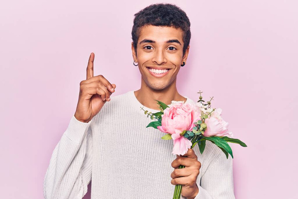 若いアフリカ系アメリカ人の男は、幸せな顔をしたアイデアや質問を指差す指で驚いて花を保持、ナンバーワン  - 写真・画像