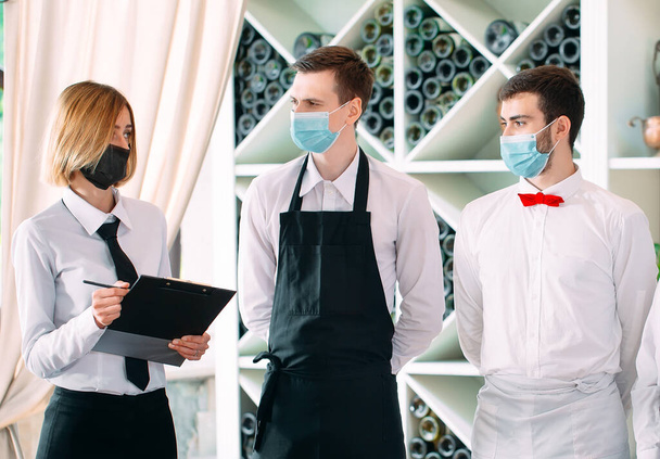 Employees of a Restaurant or Hotel in protective masks. End Of Quarantine. Restaurant Manager and his staff on the terrace. interaction with the chef in the restaurant. - Valokuva, kuva