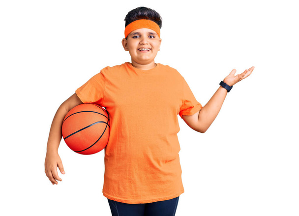 Ragazzo bambino che tiene palla da basket che celebra la vittoria con sorriso felice e l'espressione del vincitore con le mani alzate  - Foto, immagini
