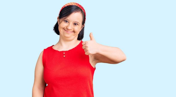 Brunette woman with down syndrome wearing casual clothes smiling happy and positive, thumb up doing excellent and approval sign  - Photo, Image