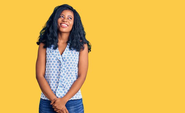 Schöne afrikanisch-amerikanische Frau in lässigem Sommerhemd, die mit einem Lächeln im Gesicht und natürlichem Ausdruck zur Seite schaut. Lachen selbstbewusst.  - Foto, Bild