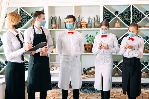 Employees of a Restaurant or Hotel in protective masks. End Of Quarantine. Restaurant Manager and his staff on the terrace. interaction with the chef in the restaurant. - Fotó, kép