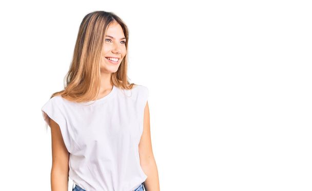 Beautiful caucasian woman with blonde hair wearing casual white tshirt looking away to side with smile on face, natural expression. laughing confident.  - Foto, Imagem