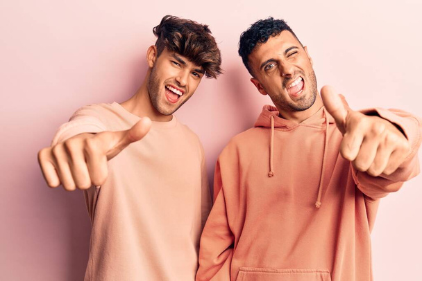 Young gay couple wearing casual clothes approving doing positive gesture with hand, thumbs up smiling and happy for success. winner gesture.  - Foto, Bild