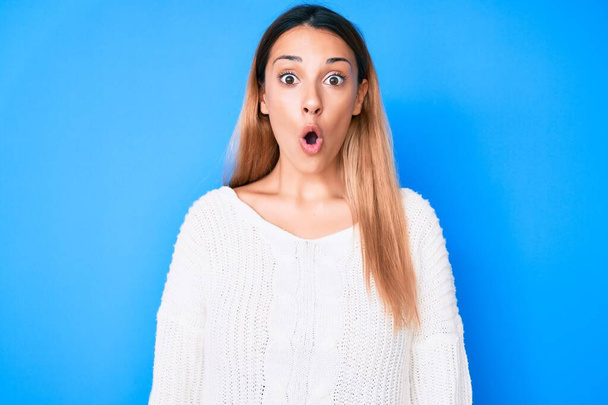 jonge brunette vrouw dragen casual trui bang en verbaasd met open mond voor verrassing, ongeloof gezicht  - Foto, afbeelding