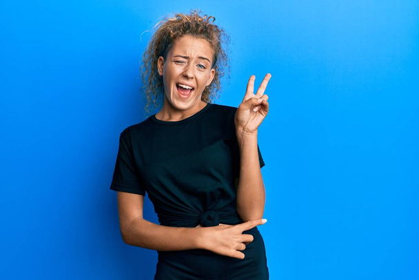 Beautiful caucasian teenager girl wearing black sportswear smiling with happy face winking at the camera doing victory sign. number two.  - Photo, Image