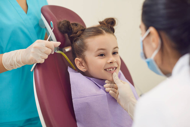Woman dentist and assistant examining smiling little girl teeth in dental clinic - Фото, зображення