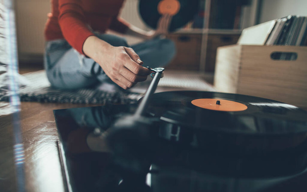 Playing vinyl record. Cropped shot of woman sitting on floor and playing music on turntable - Foto, Imagem