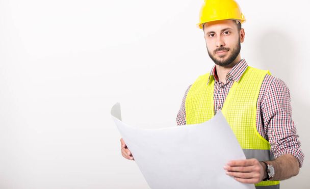 stavební dělník ve žluté přilbě a vestě pózovat na bílém pozadí - Fotografie, Obrázek