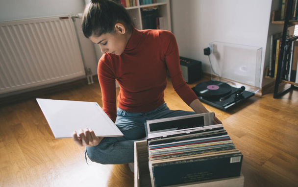 Listening vinyl records. Hipster girl searching for favourite vinyl record at her home - Фото, изображение