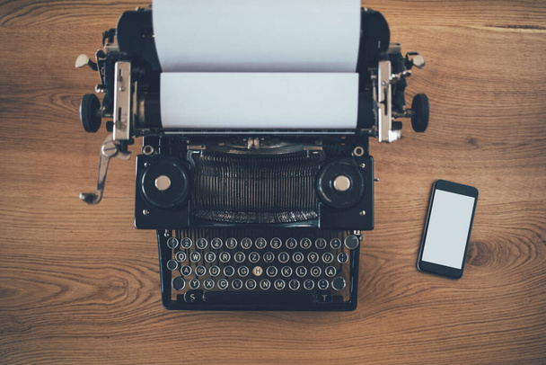 Alte Schreibmaschine mit Smartphone auf Holzgrund. Business, technologischer Fortschritt Konzept. Kopierraum - Foto, Bild