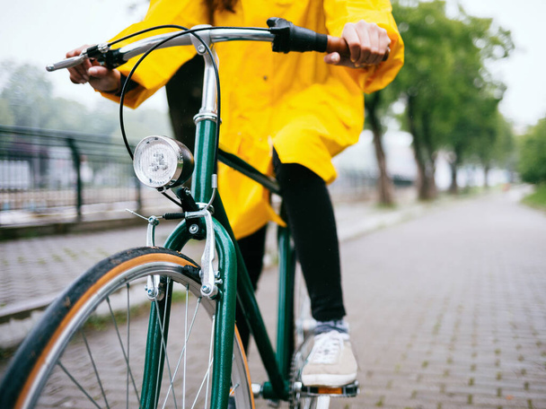Sarı ceketli genç kız parkta bisiklet sürüyor. - Fotoğraf, Görsel