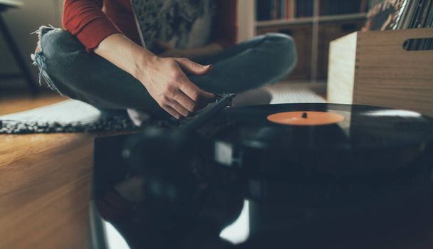 Playing vinyl record. Cropped shot of woman sitting on floor and playing music on turntable - Photo, Image
