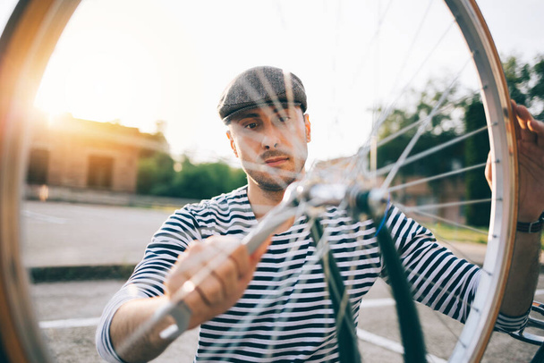 Boy in grey hat fixing bike outdoors - Valokuva, kuva