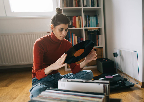 Young audiophile sitting on floor and cleaning dust form her vinyl record collection - Fotoğraf, Görsel