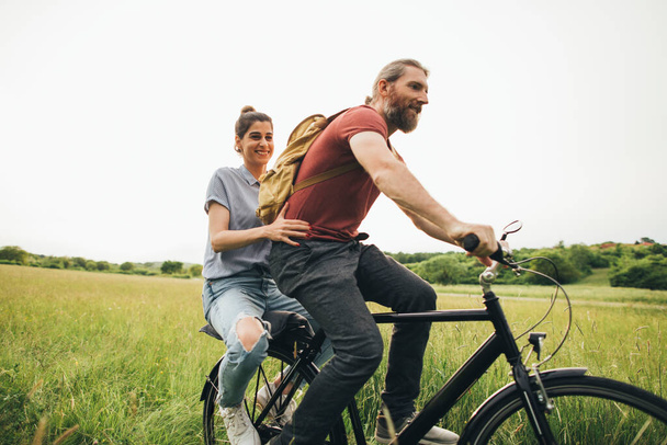 面白いカップルは夏のフィールドで自転車に乗る  - 写真・画像