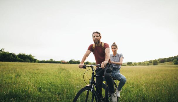 Beautiful couple ride a bike on the summer field  - Фото, зображення