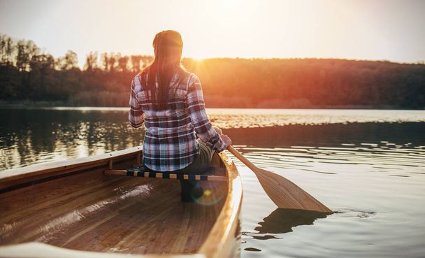 Visão traseira da mulher remando canoa ao pôr do sol  - Foto, Imagem