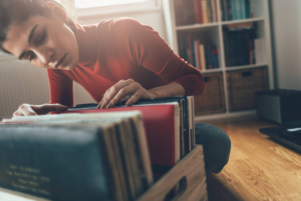 Listening vinyl records. Hipster girl searching for favourite vinyl record at her home - 写真・画像
