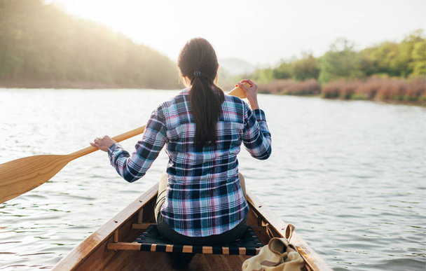 Вид сзади на девушку, катающуюся на каноэ на закатном озере - Фото, изображение