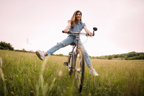 Beautiful young girl ride a bike on the green field - Photo, Image