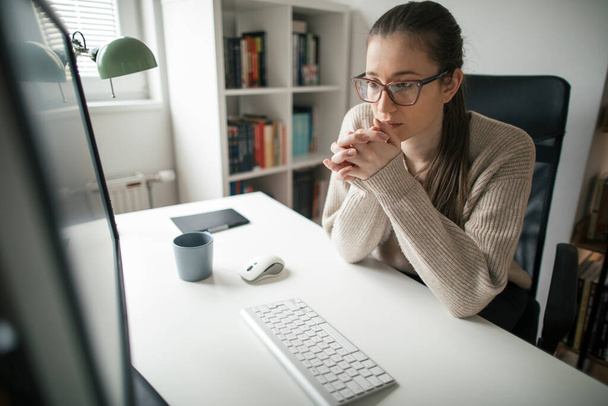 Nuori nainen työskentelee tietokoneella kotonaan. Keskittynyt nuori nainen tekee pitkiä päiviä - Valokuva, kuva