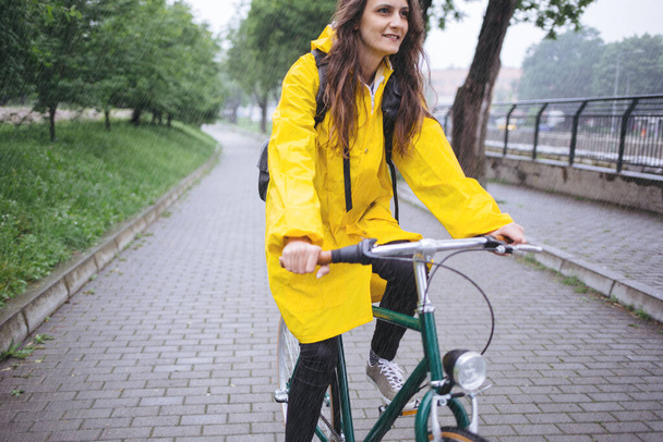 Giovane ragazza in cappotto giallo andare in bicicletta nel parco - Foto, immagini