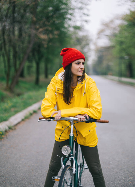 Nainen punaisessa hatussa ja keltainen takki harjaus polkupyörällä - Valokuva, kuva