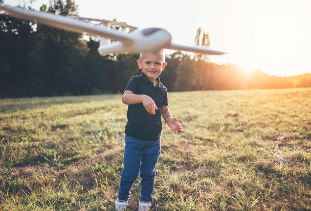 Junge spielen gerne mit Flugzeugmodell. Lächelnder Junge wirft Flugzeug und träumt vom Fliegen  - Foto, Bild