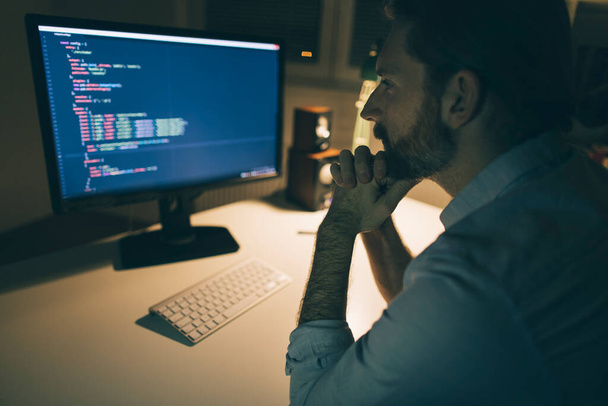 El hombre se centró en leer códigos informáticos. Programador trabajando hasta tarde desde su oficina en casa - Foto, imagen