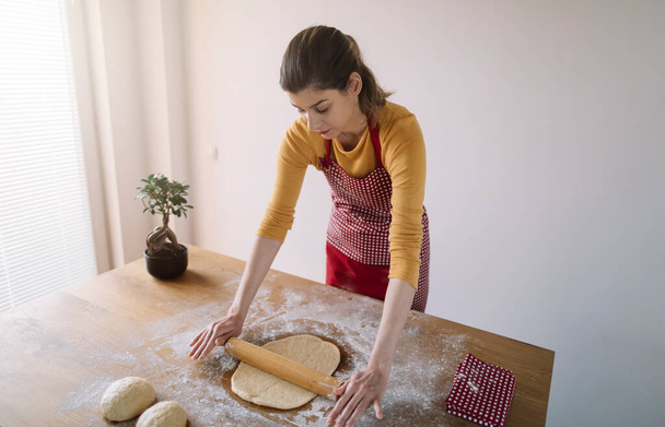 Kobieta ugniatająca chleb ciastem z wałkiem na stole kuchennym. Pieczenie domowe - Zdjęcie, obraz