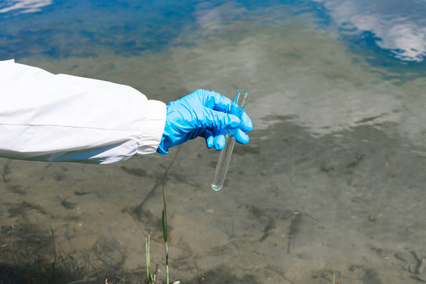 Ecologist holds a test tube with water on a background of lake, river, sea. The concept of ecology, environmental pollution - Zdjęcie, obraz