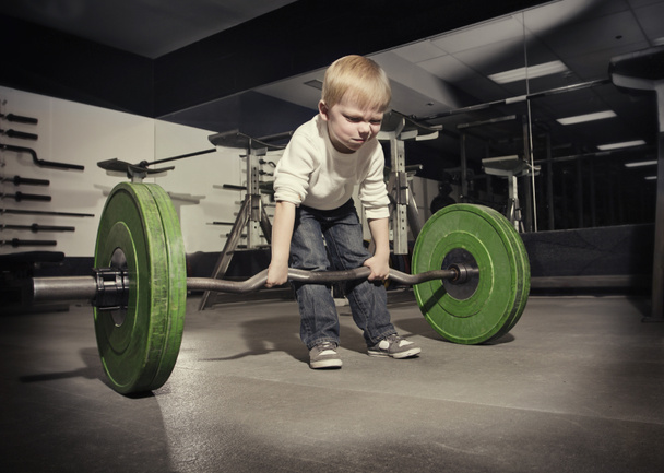 Determined young boy trying to lift a heavy weight bar - Photo, Image