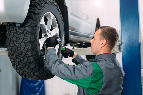 Car lifted in automobile service for fixing, worker repairs the wheel, - Фото, изображение
