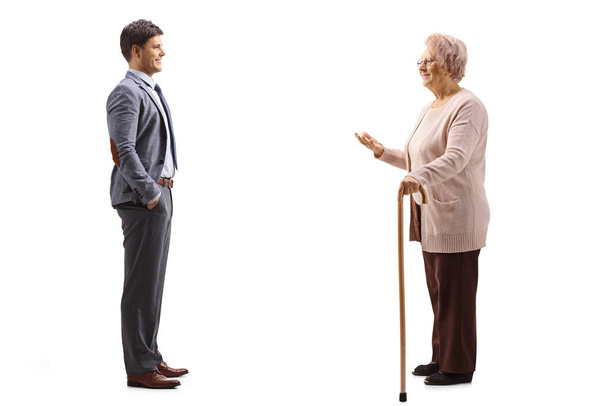 Full length profile shot of an elderly lady with a walking cane and a man standing and talking isolated on white background - 写真・画像