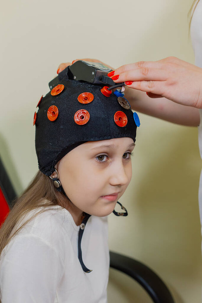 Een vrouw kinderen neuroloog onderzoekt een meisje in het kantoor met een speciaal apparaat. - Foto, afbeelding