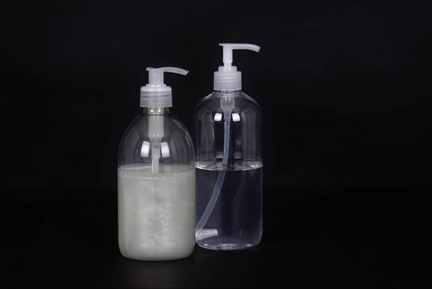 Un primer plano de jabón líquido y desinfectante de manos en botellas aisladas sobre un fondo negro - Foto, Imagen