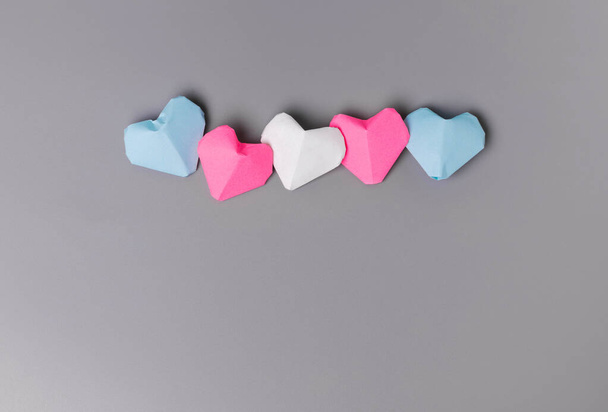 Орігамі паперові серця в трансгендерних кольорах прапора на сірому фоні
 - Фото, зображення