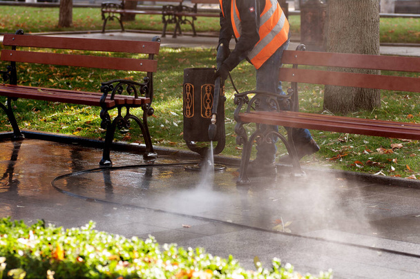 Silne ciśnienie wody, czyszczenie wodą. Pracownik czyści ulicę wodą, jesienią w parku - Zdjęcie, obraz