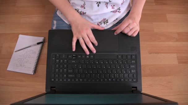 Persona se sienta en un piso de madera con un ordenador portátil, trabajando desde casa - Metraje, vídeo