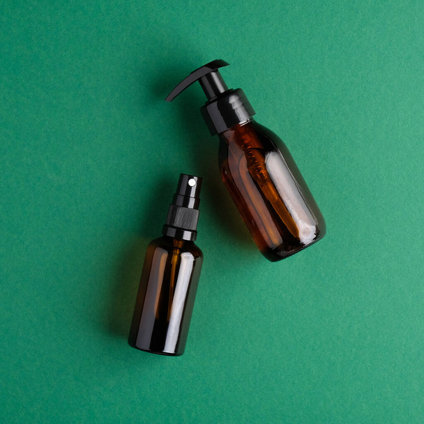 Cosmetic amber glass bottles on green background. Flat lay, top view. Natural organic beauty products packaging design. - Фото, зображення