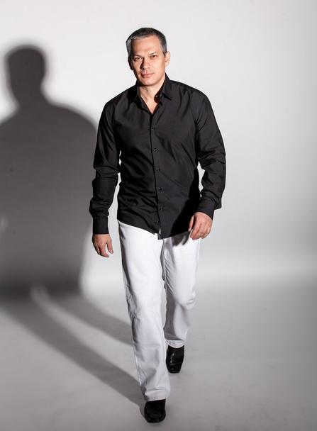 Man in black shirt and white trousers walking in studio - Фото, зображення