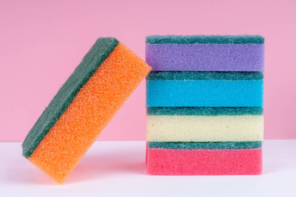 Multicolored sponges for washing dishes on top of each other on a pink background. Cleaning concept. - Фото, изображение
