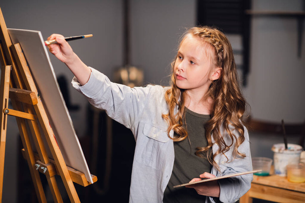 Ein kleines Mädchen zeichnet im Atelier ein Bild mit einem Pinsel. Eine talentierte junge Schülerin - Foto, Bild