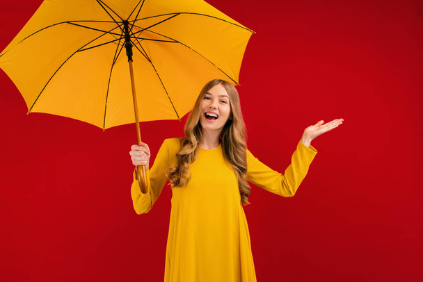 Shocked happy beautiful young woman, with a yellow umbrella on a red background, autumn concept - Valokuva, kuva